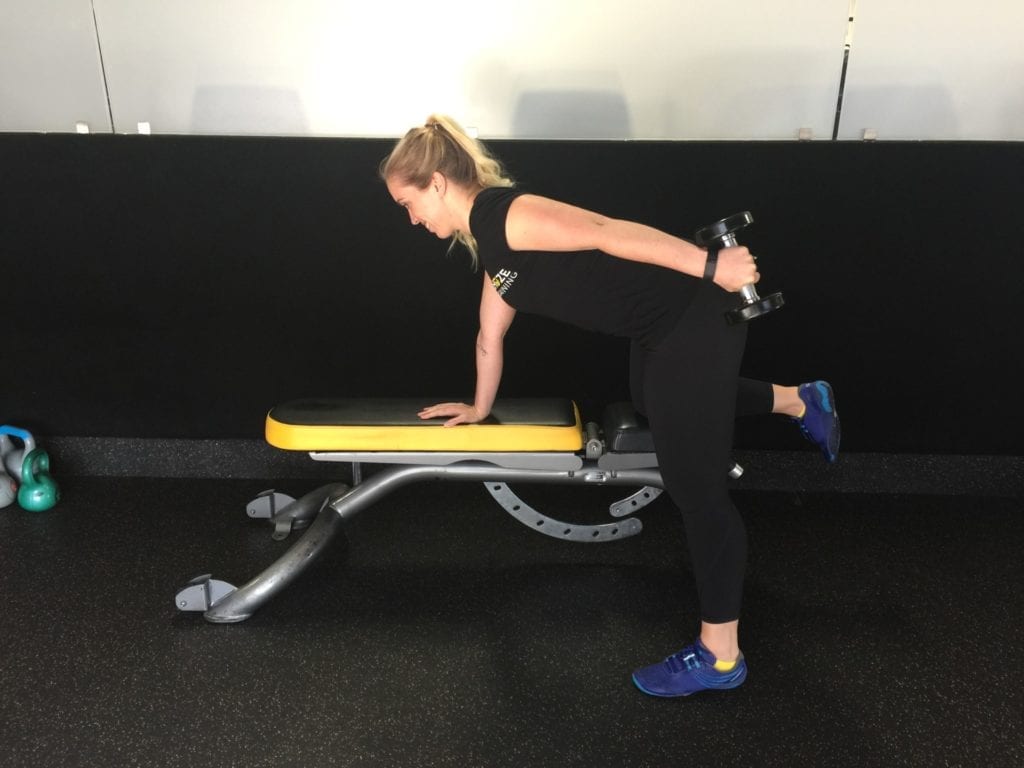 Personal trainer performing tricep kickbacks on bench